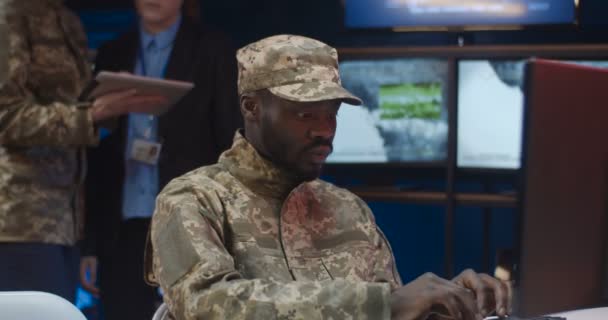 Close up of African American young man in camouflage uniform and cap sitting at laptop computer and typing on keyboard in monitoring room in army. Soldier working in military center. — Stock Video