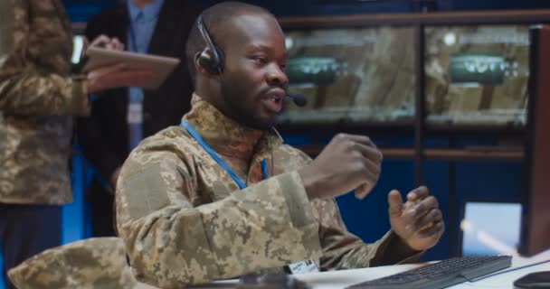 Jonge Afro-Amerikaanse militaire officier in uniform en headset met microfoon zittend achter de computer en pratend via webcam. Man in het leger spreekt op video oproep in het kantoor. — Stockvideo