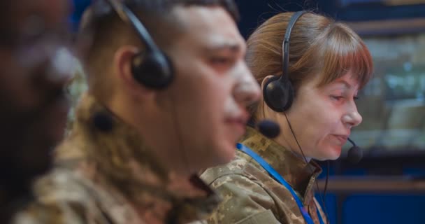 Großaufnahme eines kaukasischen Offiziers im Headset, der als Disponent im Überwachungsraum arbeitet. Soldat, der Anrufe über die Hotline der Armeeleitstelle entgegennimmt. Multiethnische männliche und weibliche Mitarbeiter neben. — Stockvideo