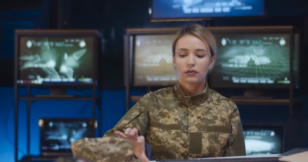 Ritratto di una bella soldatessa caucasica seduta alla scrivania nella sala di monitoraggio, che prende il berretto e guarda la telecamera. Donna attraente in uniforme militare che lavora nelle truppe. Ragazza nel concetto di esercito . — Video Stock