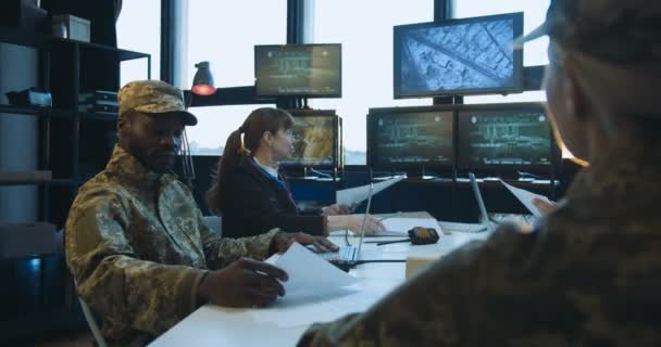 Concepto de conferencia de tropas. Soldados y generales de razas mixtas masculinos y femeninos sentados alrededor de la mesa y mirando la pantalla mientras planifican la operación militar . — Vídeos de Stock