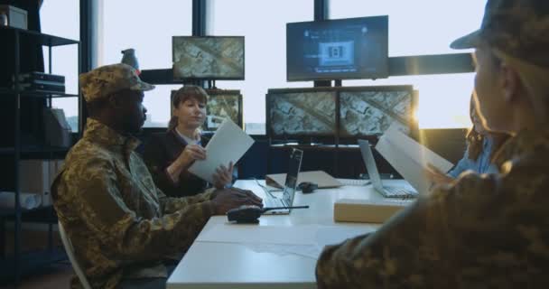 Зустріч військових чоловіків і жінок, які вирішують серйозні питання армії. Жінка роздає секрети документи чоловікам і жінкам у формі, які обіймають стіл . — стокове відео