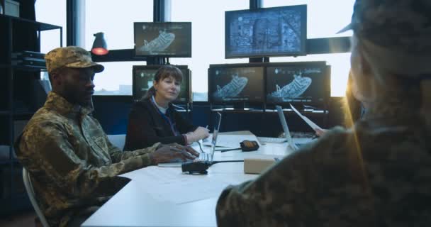 Blick über die Schulter der kaukasischen Blondine am Tisch mit Mann und Frau in Uniform, die auf den Bildschirm schauen und die Truppenverlegung bei einem Militärtreffen entscheiden. — Stockvideo