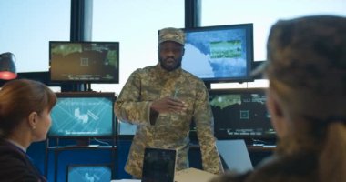 Afrika kökenli genç ordu generali asker toplantısında beyaz kadınlarla konuşuyor. Konuşan adam askeri konferansta kadın meslektaşlarına rapor veriyor. Askeri Yerdeğiştirme Konsepti.