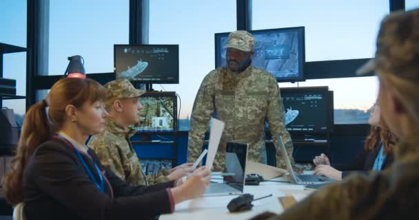 Αφρο-αμερικάνος κυβερνά τις στρατιωτικές συναντήσεις και μιλάει για την έκθεση του σχετικά με την επαγγελματική πληροφόρηση. Καυκάσιος αρσενικό και θηλυκό στρατιωτικό προσωπικό ακούγοντας ομιλία του αφεντικού και μελετώντας έγγραφα. — Αρχείο Βίντεο