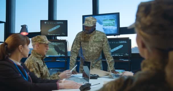 Sede geral sob a régua do homem afro-americano que toma a decisão militar na reunião de pessoal no escritório com telas e computadores de altas tecnologias. Homens e mulheres multiétnicos no exército . — Vídeo de Stock