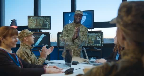 Homem afro-americano, jovem chefe no exército terminando conferência militar no escritório com telas e pessoal aplaudindo os oradores. Pessoal multiétnico masculino e feminino das tropas na reunião . — Vídeo de Stock