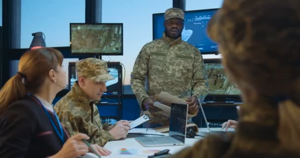 Ein junger afroamerikanischer Mann, Chef des Hauptquartiers, kommt herein und übergibt den Arbeitern der kaukasischen Truppen Dokumente mit Aufgaben. Metting über Armeestützpunkt und Planung. Brainstorming der Armeeoperation. — Stockvideo