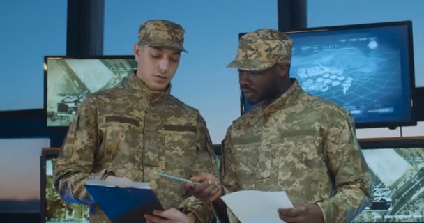 Blandade raser manliga soldater i uniformer talar i ämbetet med skärmar och datorer. Kaukasiska och afroamerikanska militärer läser dokument och skakar hand när de säger adjö. — Stockvideo