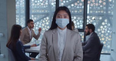 Ofiste kameraya bakan koruyucu maske takan Asyalı genç bir iş kadınının portresi. Sağlık ve güvenlik hayatı kavramı, koronavirüs, virüs koruması, salgın hastalık.