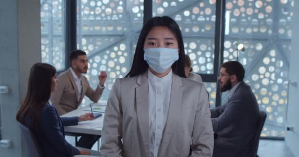 Portret młodej azjatyckiej biznesmenki w masce ochronnej, patrzącej przed kamerą w biurze. Pojęcie bezpieczeństwa i higieny pracy, koronawirusy, ochrona przed wirusami, pandemia. — Wideo stockowe