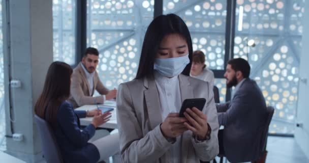 Retrato de una joven mujer de negocios asiática con máscara protectora usando un teléfono inteligente en la oficina. Concepto de vida en materia de salud y seguridad, coronavirus, protección contra virus, pandemia . — Vídeos de Stock