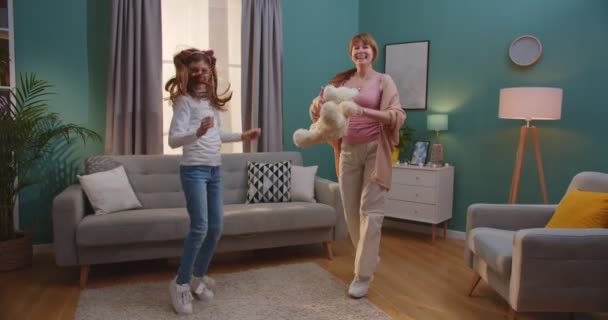 Kavkazský šťastný matka a dospívající roztomilé dcera tanec a baví v útulném obývacím pokoji. Krásná žena a malá dívka tráví den-off spolu doma s hudbou. — Stock video