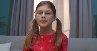 Beyaz tenli, gözlüklü, genç ve güzel bir kızın kameraya bakıp gülerken evdeki kanepede oturması. Oturma odasındaki kanepede küçük mutlu bir çocuğun portresi..