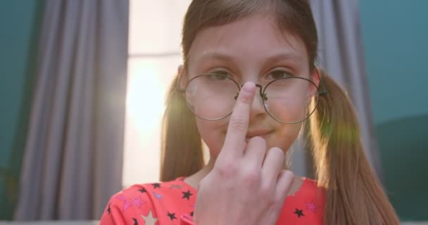 Retrato de linda niña adolescente caucásica con dos colas y en gafas mirando en cámara y sonriendo alegremente en casa. Primer plano de la cara feliz de niño pequeño interior . — Vídeos de Stock