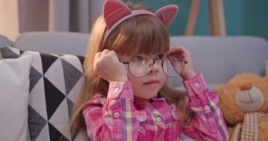 Kafkasyalı, komik kulaklı, kanepede oturan ve gözlük takan küçük şirin bir çocuk. Küçük sevimli çocuk gülümseyerek masal kitabı okuyor. Kız evde masal okurken eğleniyor ve gülümsüyor..