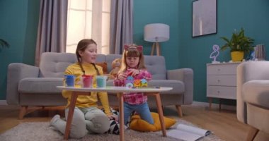 İki Kafkasyalı küçük kız rahat bir odada masada oturmuş oynuyorlar. Büyük kız kardeş küçük kızla vakit geçiriyor ve oyununu evde oynuyor. Mutlu çocukluk arkadaşlarla.