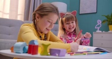 Neşeli küçük beyaz kız kardeşler evde yalnız oturuyor ve birlikte iyi geçiniyorlar. Şirin çocuklar resim boyuyor. Odalarında renkli kalemler var. Mutlu çocuklar içeride oynar ve konuşurlar..