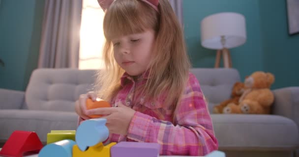 Миле кавказьке дитя бавиться з дитячими іграшками з барвистими кубиками за столом у затишній вітальні. Весела гарна дівчина розважається в приміщенні. Діти проводять час удома наодинці.. — стокове відео