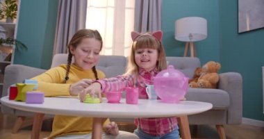 Kafkasyalı mutlu ve şirin küçük kızlar rahat oturma odasında bebek masalarıyla oynuyorlar. Küçük kız kardeşler içeride birlikte oynarlar. Çocuklar evde yalnızken birlikte oynuyorlar..