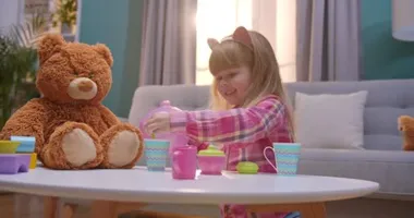 Kafkasyalı şirin kız rahat oturma odasında bebek sofra takımıyla oynuyor. Küçük çocuk oyuncak ayısı için çaydanlıktan çaydanlığa hayali çay dolduruyor. Evde yalnız başına oynayan çocuk..