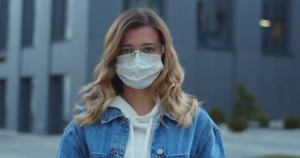마스크를 쓰고 밖에서 카메라를 보고 있는 여성의 사진. 건강 과 안전 , n1h1 코로나 바이러스, 바이러스 보호 치료 및 의학 개념. 거리에서 의료용 마스크를 쓰고 있는 소녀. — 비디오