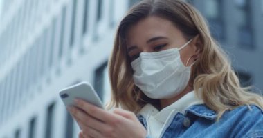 Şehirde maskeli akıllı telefon takan bir kadın. Sağlık ve güvenlik, N1H1 koronavirüs, virüs koruma ve tıbbi konsept. Sokakta koruyucu tıbbi maskeli genç bir kızın portresi..