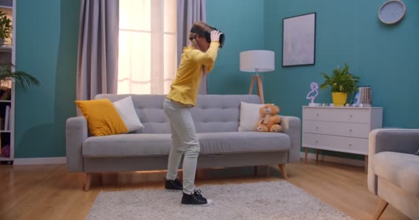Caucasian cute teen girl in VR glasses standing in living room and playing  in virtual reality like touching and grabing things. Funny joyful child  having headset indoor. World of virtuality concept. —