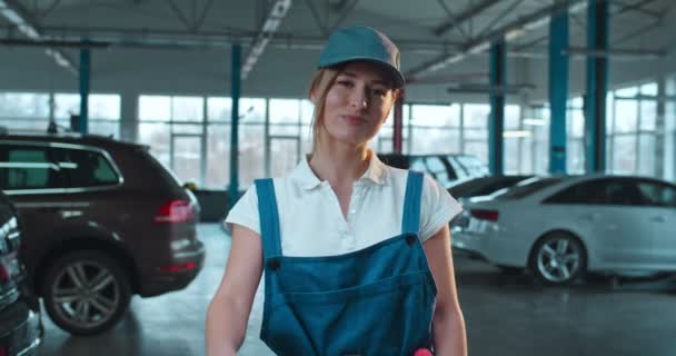 Retrato de feliz alegre caucásico hermosa mujer mecánico de automóviles sonriendo a la cámara y dando pulgar hacia arriba en el garaje. Joven chica bonita en overoles y sombrero en el garaje de servicio de coches . — Vídeos de Stock