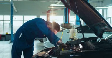 Beyaz tenli yakışıklı otomobil mühendisi açık arabada duruyor ve büyük atölyede motorunu tamir ediyor. Üniformalı ve gözlüklü bir erkek, kapalı otoparkta çalışıyor. Taşıma hizmeti kavramı.