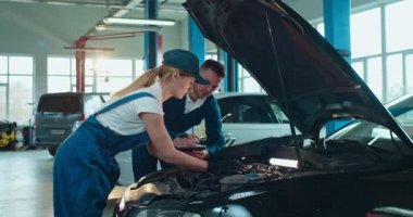 Kafkasyalı bir adam araba tamirhanesinde genç bir bayana tulum ve şapka öğretiyor. Erkek meslektaşım yardım ve kontrol ederken, kadın işçi büyük garajda motor öğreniyor ve tamir ediyor..