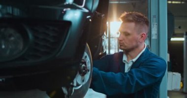 Beyaz tenli yakışıklı bir adam, araba tamirhanesinde çalışırken pahalı bir arabanın tekerleğini tamir ediyor. Tamirat sırasında erkek tamirci otomobilde bazı ayrıntıları şişiriyor..