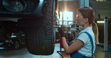 Garajda çalışan ve tekerlekleri tamir eden beyaz, genç bir kadın. Otomobil tekerleklerini kontrol eden bir kadın var. Araç atölyesi konsepti. Gözlüklü kızın portresi.