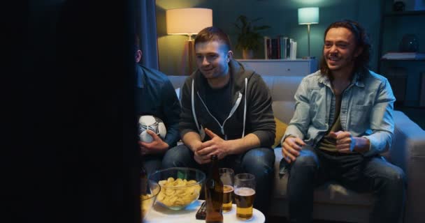 夜にはソファに座って、好きなサッカーチームのために感情的に応援するサッカーファンは、テレビで試合を見ている。テレビ画面でゲーム結果を心配してビールを持つ男性. — ストック動画