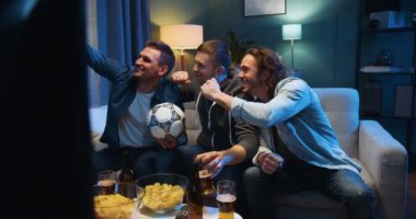 Üç neşeli Kafkas dostu adam geceleri kanepede futbol topu, abur cubur ve bira ile oturuyor ve akıllı telefon kamerasıyla selfie çekiyorlar. Spor hayranları televizyondaki oturma odasında telefonla konuşuyorlar..
