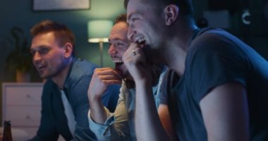 Gecenin geç saatlerinde evdeki kanepede oturan ve televizyonda komedi filmi izleyen neşeli beyaz adamları yakın çekim. Neşeli adamlar gülüyor. Erkek kankalar birlikte vakit geçirir ve spor kanallarını izlerler..