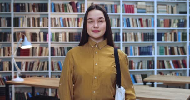 Porträtt av miljövänlig brunett student med vit väska samla in information från olika böcker i biblioteket. — Stockvideo