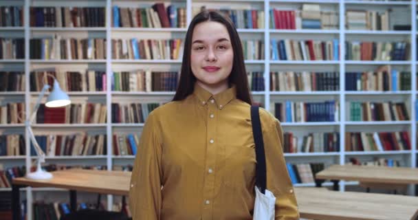 Portret der umweltfreundlichen brünetten Studentin mit weißer Tasche, die Informationen aus verschiedenen Büchern in der Bibliothek sammelt. — Stockvideo