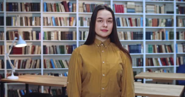 Portret de fille mignonne en pull jaune et noir cheveux longs collecte de données pour le papier dans la bibliothèque . — Video