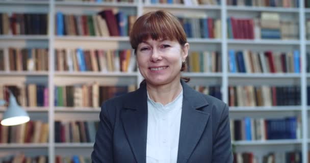 Retrato de cerca de una empresaria profesional sonriendo y mirando la cámara en la biblioteca junto al estante del libro . — Vídeo de stock