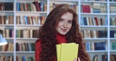 Kütüphanede çalışan kızıl saçlı, uzun kıvırcık saçlı ve sarı kitaplı güzel bir kızın portresi. Arkaplanda kitaplık.