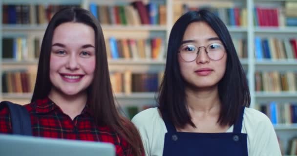 Retrato de estudantes de raça mista amigável se preparando para exames na biblioteca. Meninas olhando para a câmera e sorrindo . — Vídeo de Stock