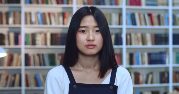 Portrait of beautiful scared youngasian girl crossing her hends and saying no in library.Bookcase in background. — Stock Video