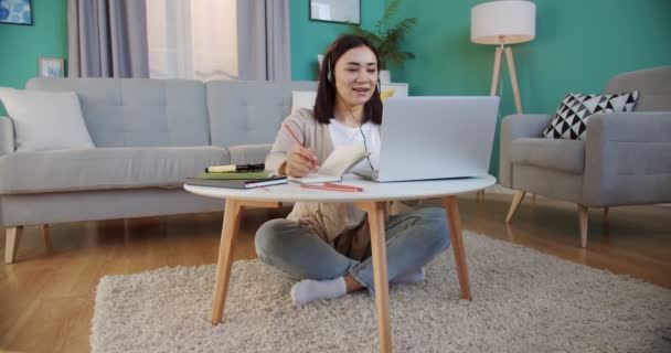 Female freelancer working on laptop, speaking with clients using headsets and making notes in paper notebook . Woman search for information using laptop computer in home interior. — Stock Video