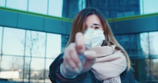 Sokakta koruyucu maske takan ve el dezenfektanı kullanan neşeli bir kızın portresi. Sağlık ve güvenlik hayatı kavramı, koronavirüs, virüs koruması, salgın hastalık — Stok video