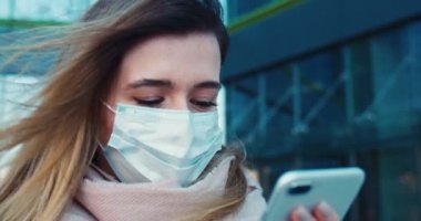 Boş sokaklarda koruyucu maske takıp telefonuyla mesajlaşan güzel bir kızın portresini yakından çek. Sağlık ve güvenlik kavramını, koronavirüs karantinasını, virüs korumasını