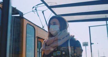 Tıbbi maskeli genç ve güzel bir kızın toplu taşıma durağında durup tramvayı beklediği portreyi yakından çek. Sağlık ve güvenlik kavramını, koronavirüs karantinasını, virüs korumasını