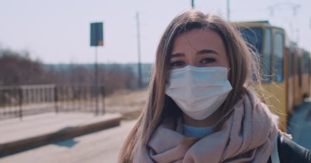 Close-up portret van een vrouw met een chirurgisch masker en wachtend op het tramstation. Mensen gebruikten maskers als voorzorgsmaatregelen tijdens het coronavirus. Concept gezondheid en veiligheid, coronavirus quarantaine. — Stockvideo