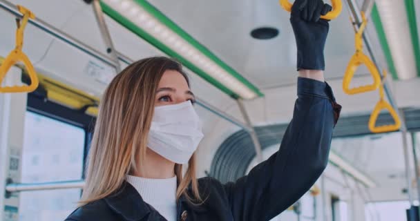 Närbild porträtt av vacker kvinna i en medicinsk mask rider i en tom spårvagn bil och tittar i fönster. Står och håller i ledstången. Coronavirus överföring i kollektivtrafiken. — Stockvideo