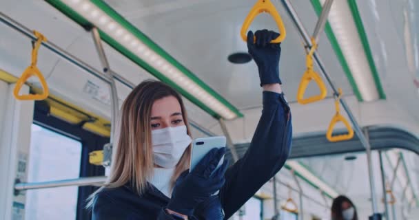 Close up retrato de jovem estudante assustado em uma máscara médica e luvas está lendo notícias em seu telefone no ônibus. Quarentena COVID-19 na Europa. Transmissão do vírus da coronária nos transportes públicos . — Vídeo de Stock